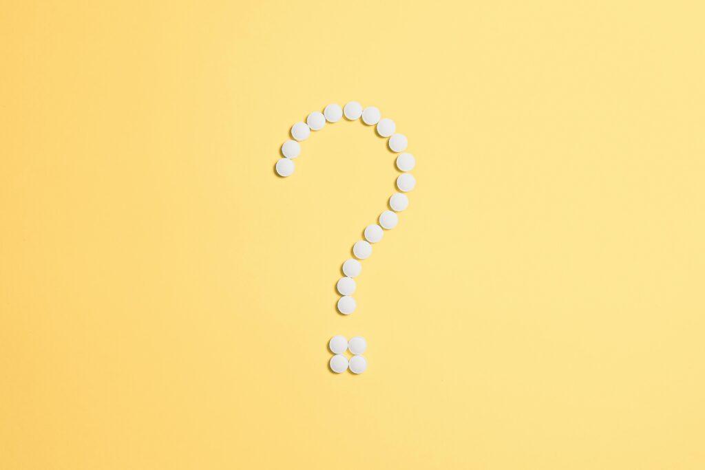 White pills arranged into a question mark shape on a vibrant yellow background.