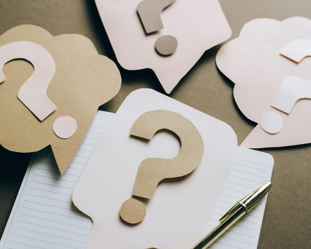 Artistic paper question marks on an open notebook with a pen, symbolizing curiosity and creativity.