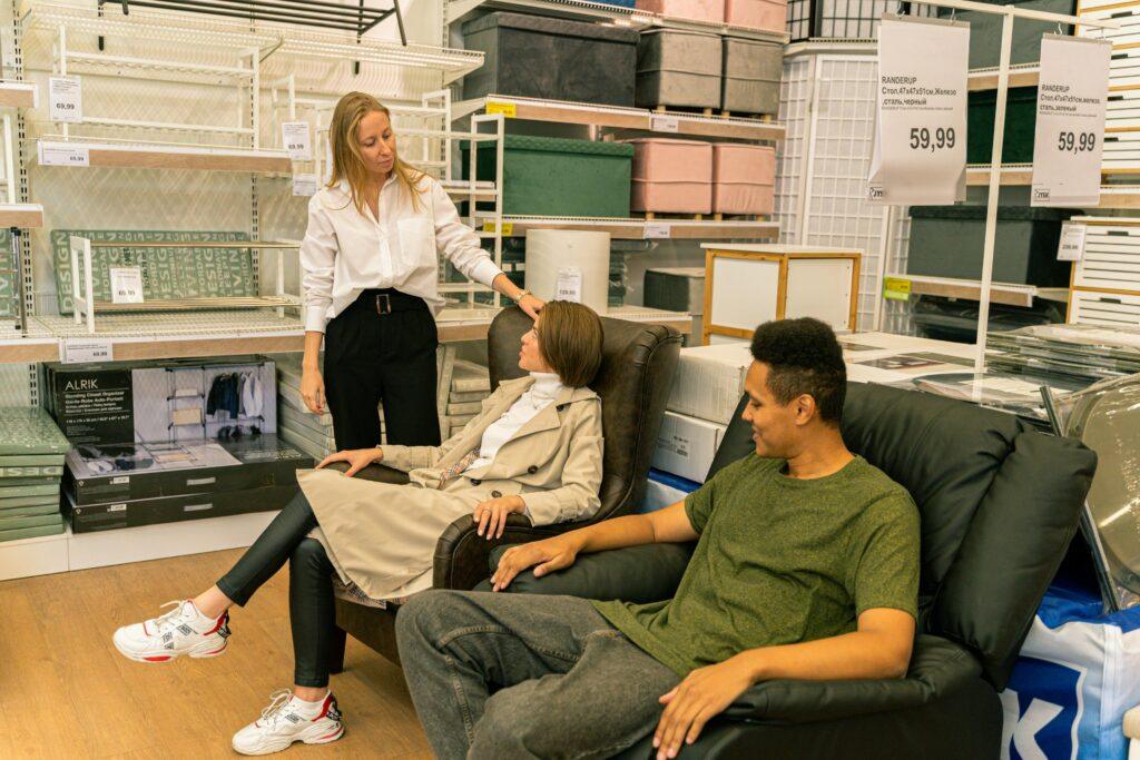 Shoppers try out leather chairs in a modern home furnishings store, guided by a salesperson.