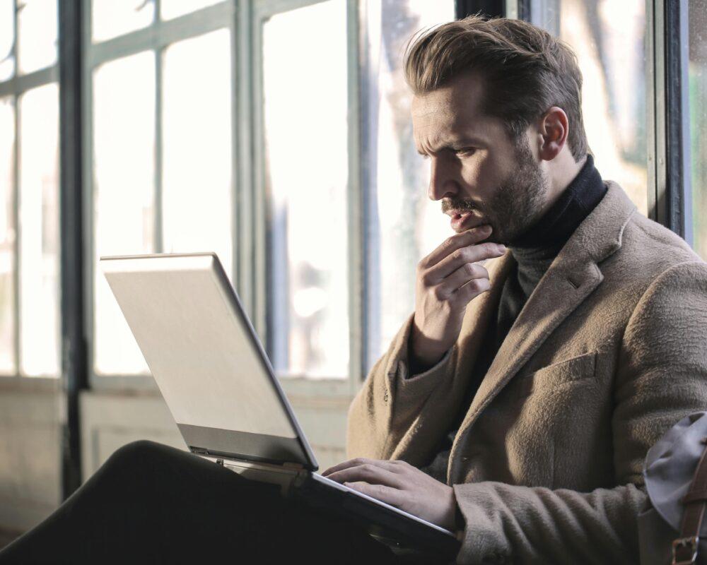 Man looking contemplative while working on a laptop in a well-lit indoor space.