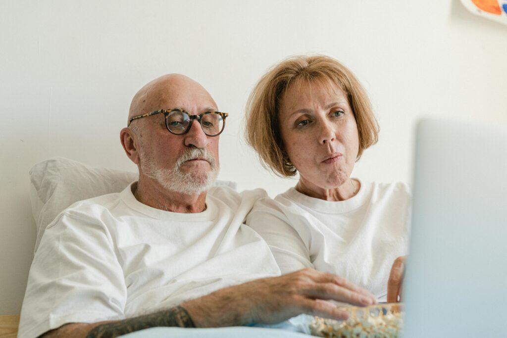 Senior couple in bed watching content on a laptop together, enjoying leisure time.